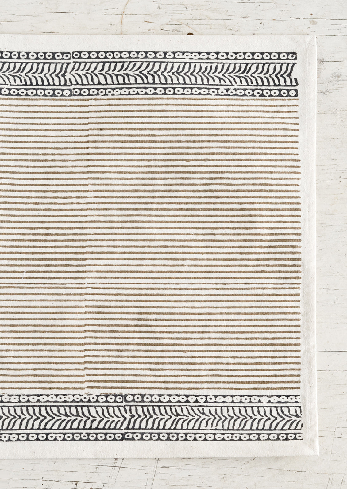 A cotton placemat with block print design, indigo borders at top and bottom with taupe striped center.