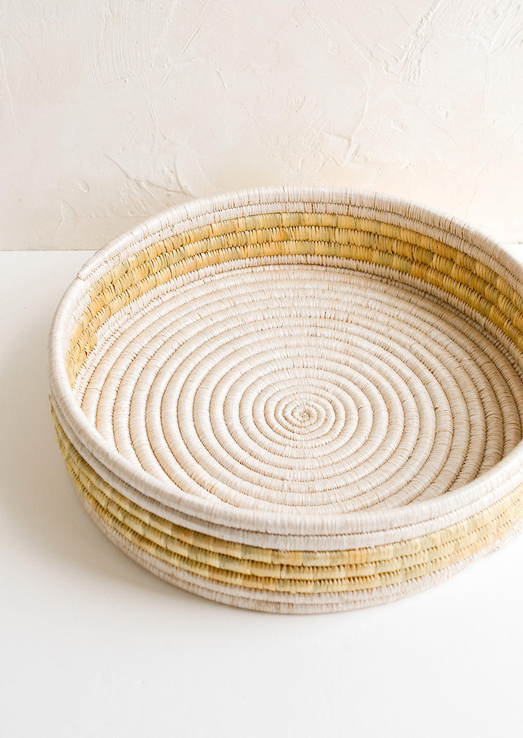 3: A round, shallow woven seagrass tray in white and beige.