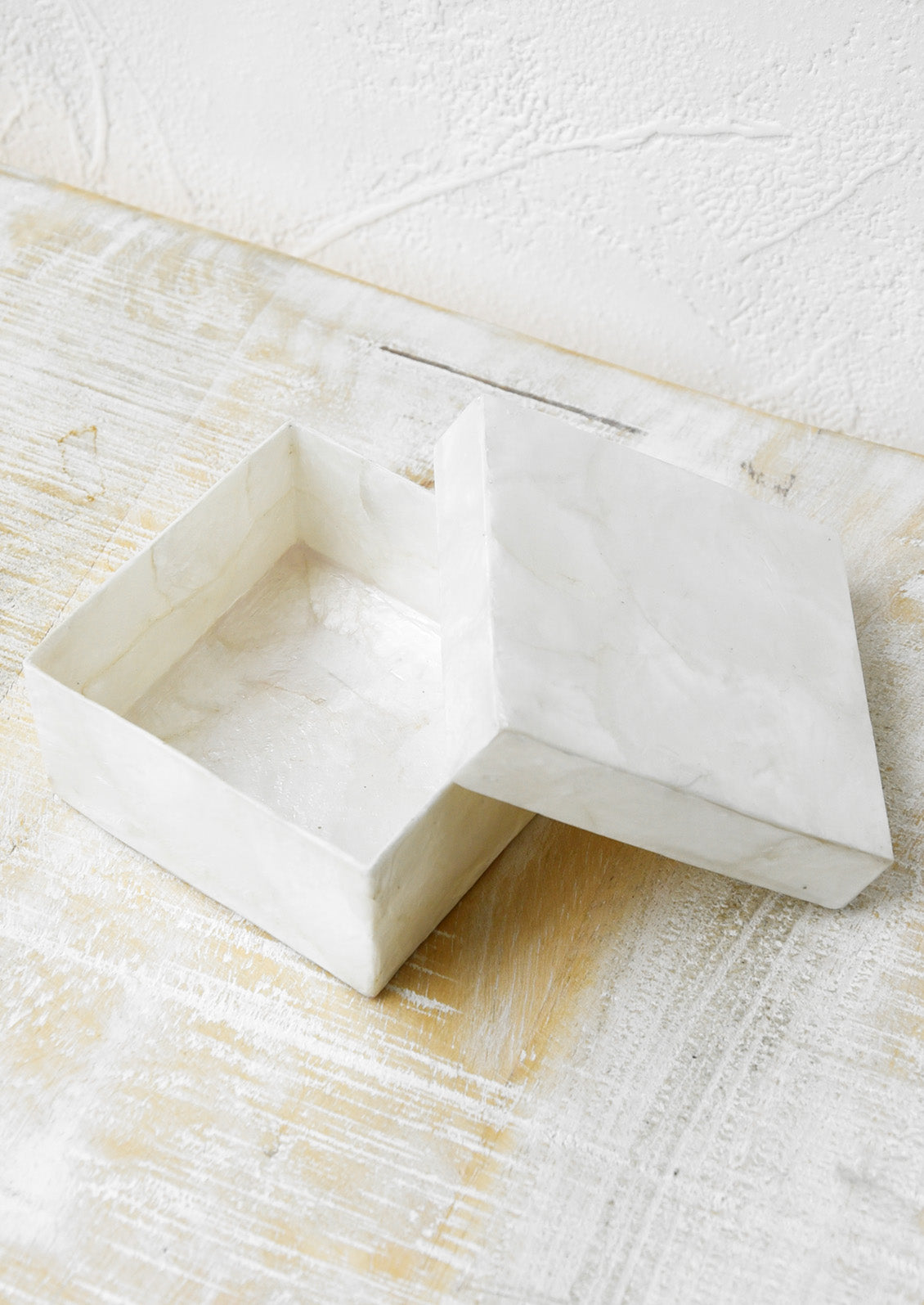 A small square box made from natural toned capiz with the lid sitting open.