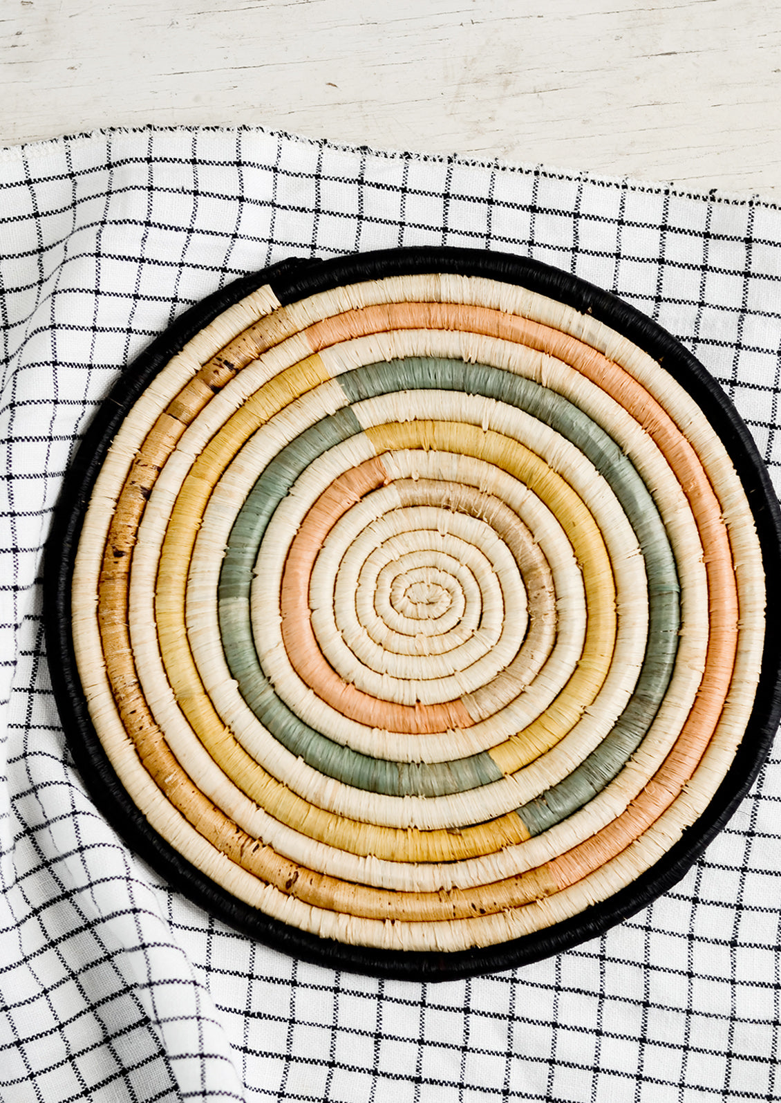 A round natural fiber trivet in pastel and black colorblock design.