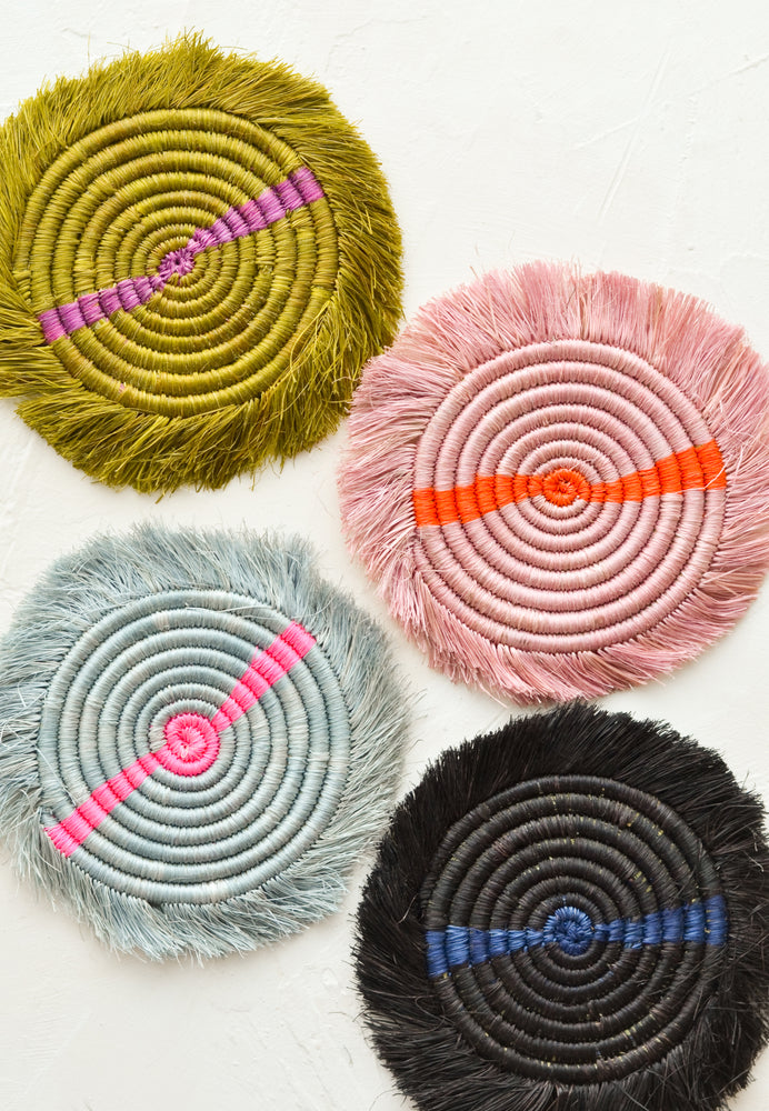 Four round sweetgrass drink coasters in two-tone neon colors with fringed trim.