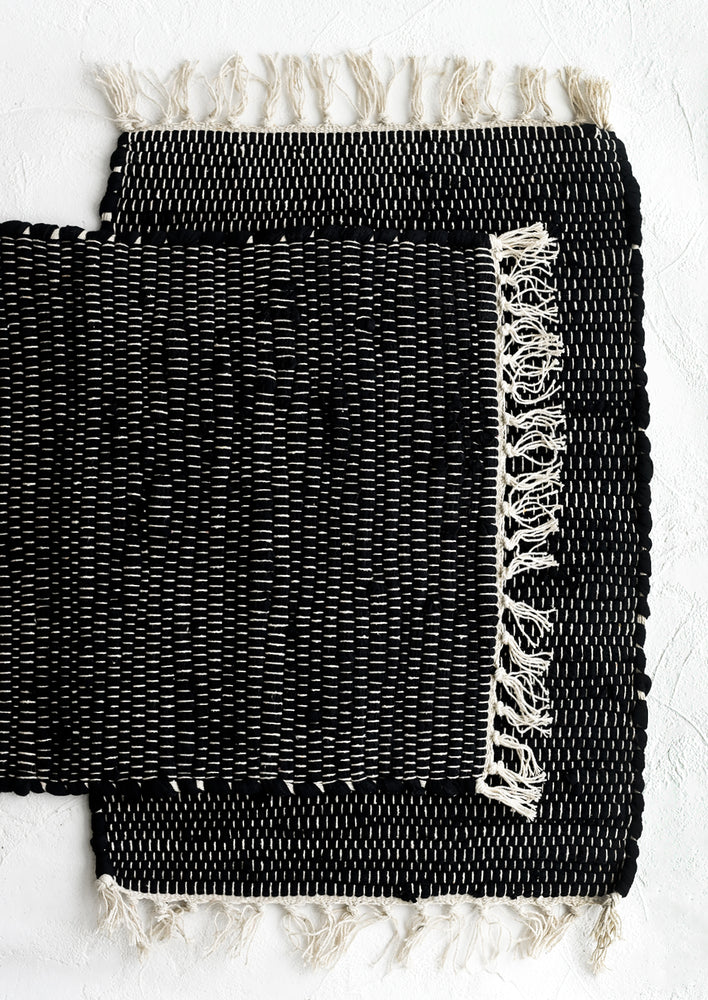 1: A black chindi weave placemat with white stitching and tassel trim.