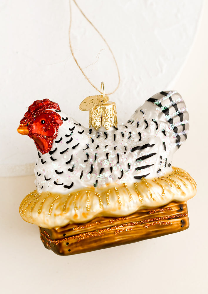 A holiday ornament of a black and white hen sitting on a nest.