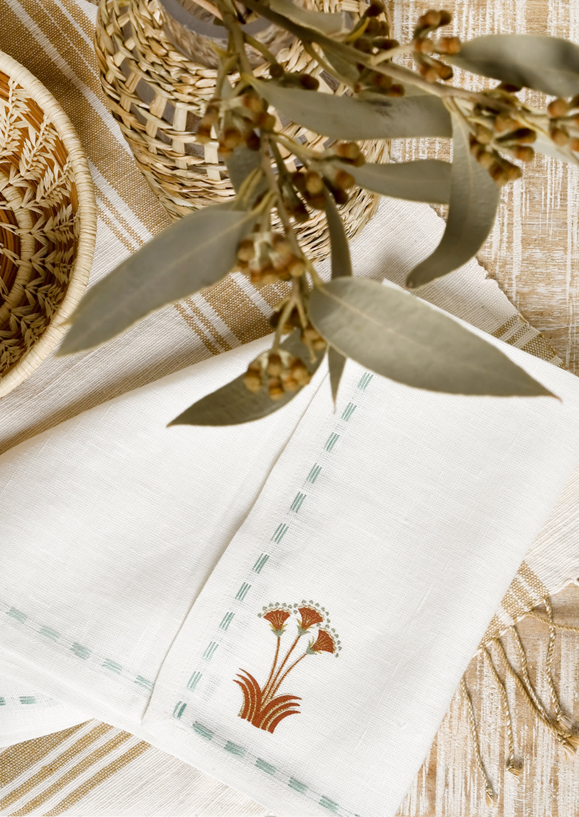 A white linen napkin with stitched seafoam border and nile lotus emblem at corner.