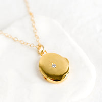 1: A gold locket necklace with north star crystal on front.
