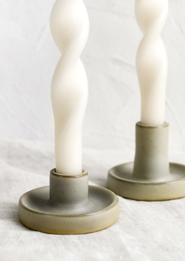 1: A pair of muted mossy green taper holders with white candles.