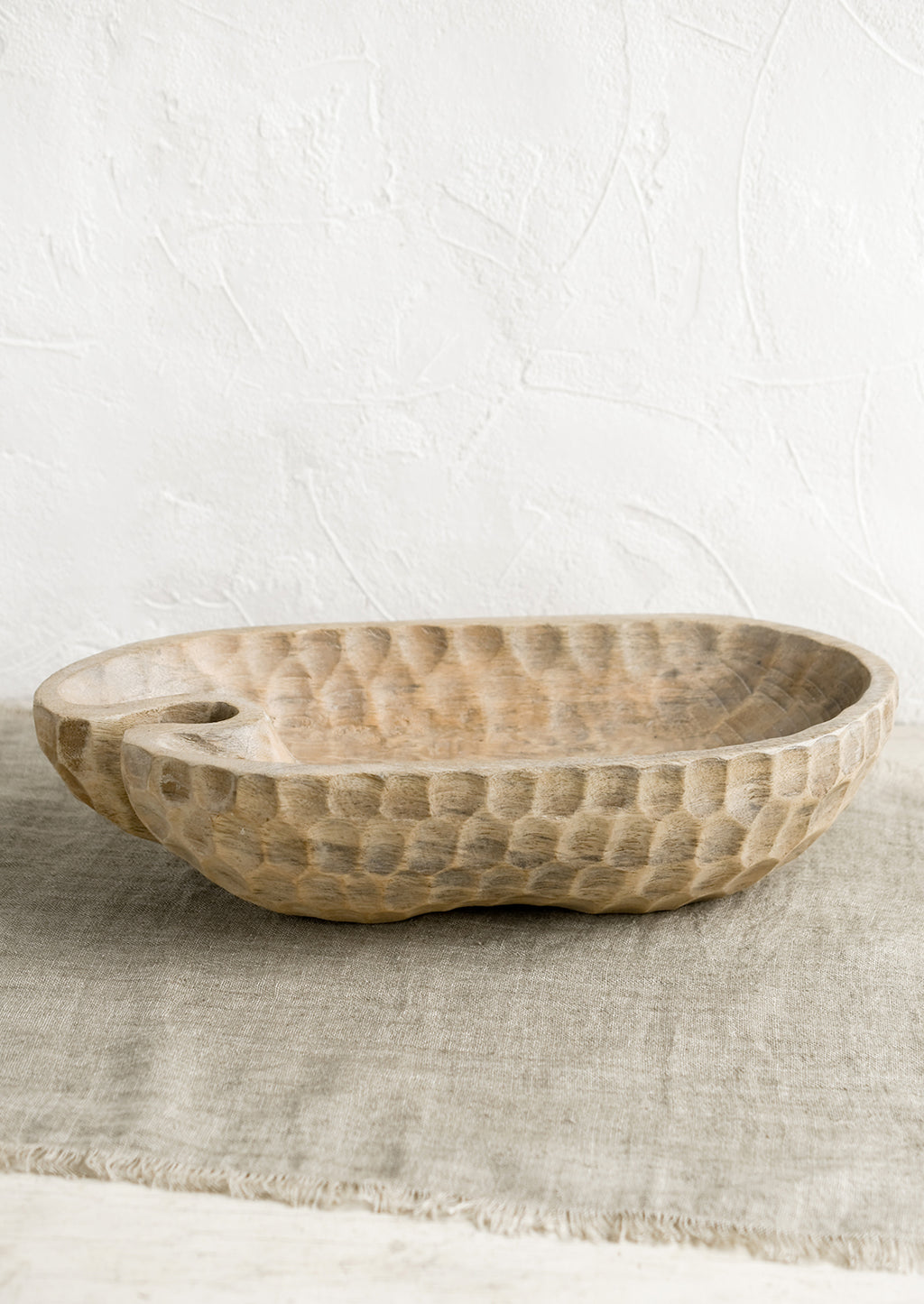 2: A light wooden bowl in organic, oblong shape, with notched texture.