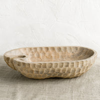 2: A light wooden bowl in organic, oblong shape, with notched texture.