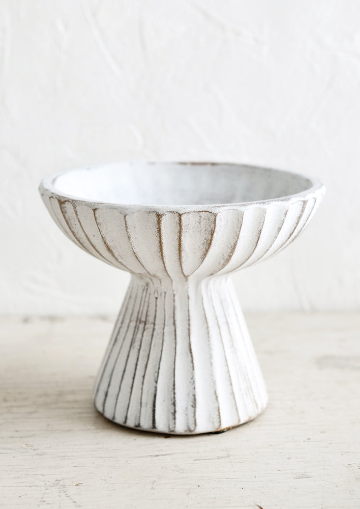 1: A ceramic pedestal bowl in distressed white ceramic with groove texture.