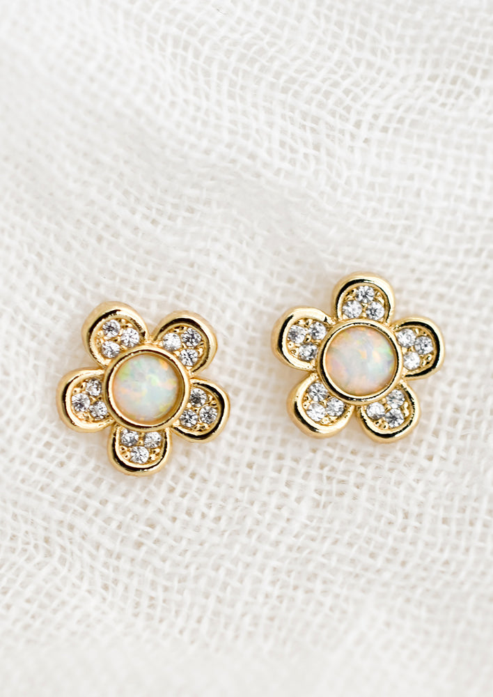 A pair of gold flower shaped stud earrings with crystal petals and opal center.
