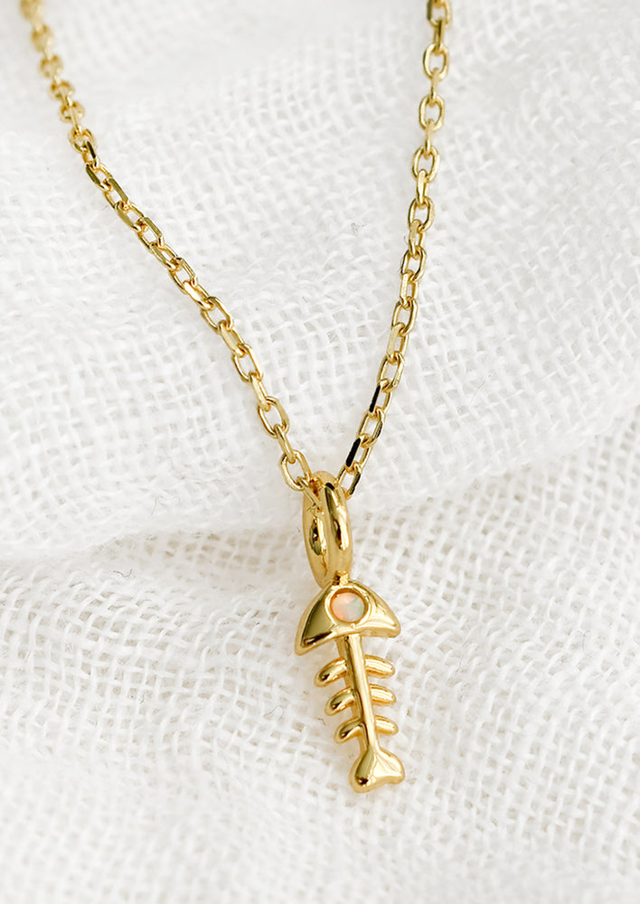 A gold tone necklace with fish bone charm with opal eye.