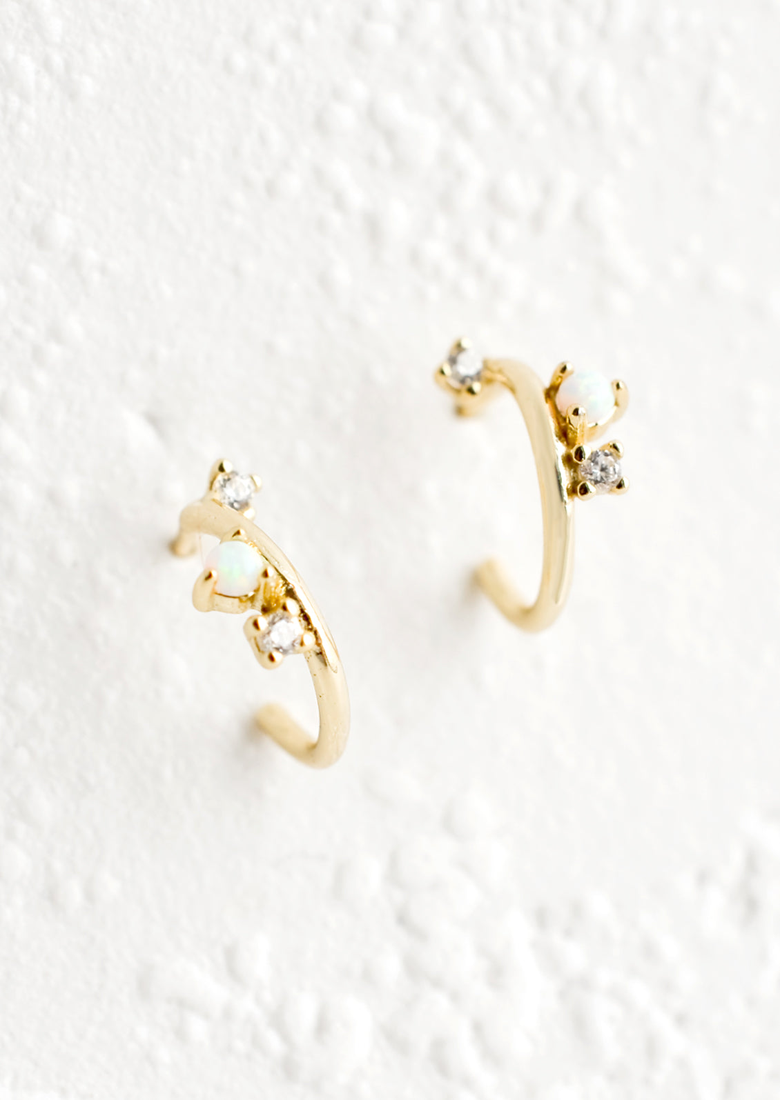 A pair of gold huggie hoop earrings with post back and opal and crystal accents