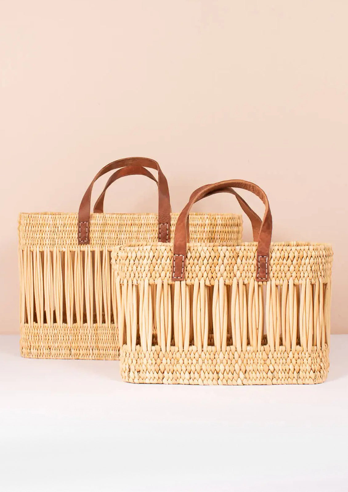 A tote-shaped woven reed basket with open air design, brown leather handles.