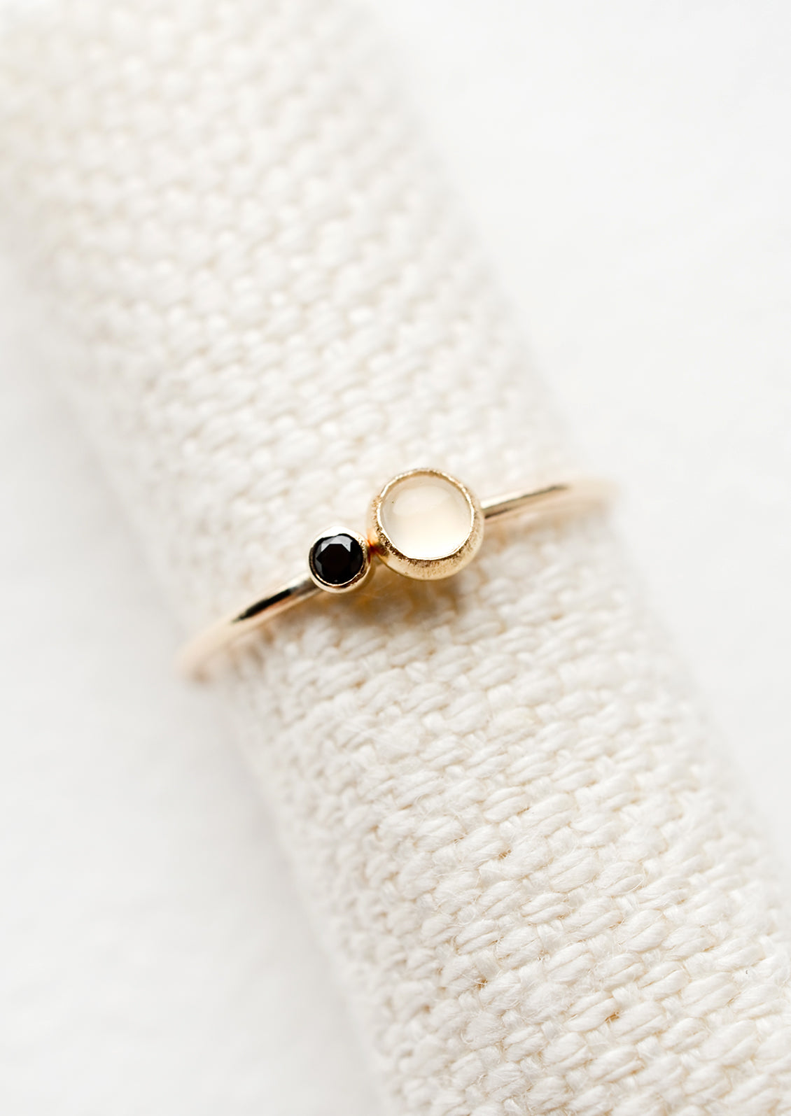 A gold ring with slim band and bezel set moonstone and black CZ.
