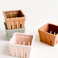 1: Ceramic baskets in the style of disposable berry baskets, shown in assorted muted hues.