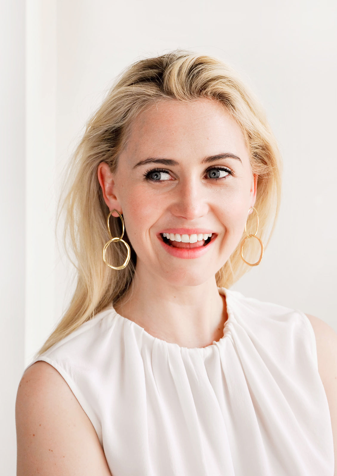 Model wears gold drop earrings and white blouse.