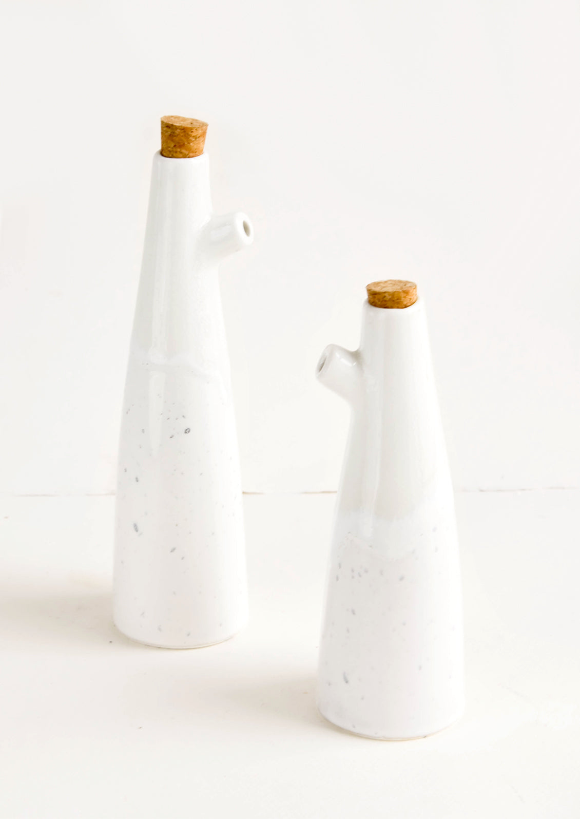 Ceramic cruets for oil & vinegar, one taller than the other. Glossy white glaze, cork stopper as lid.