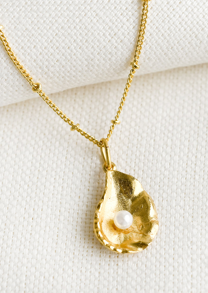 1: A gold necklace with oyster shell and single pearl inside shell.