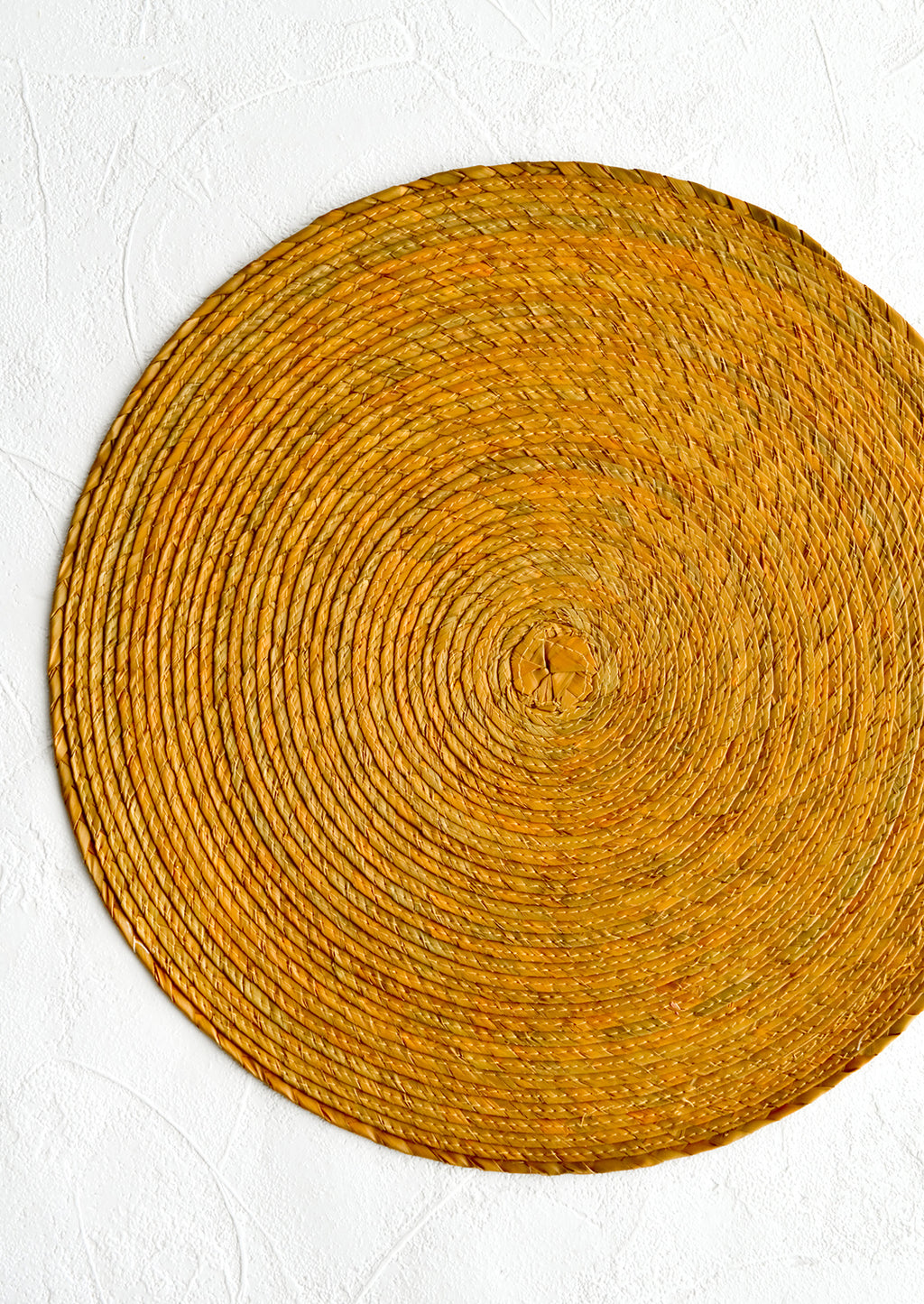 Ochre: A round woven straw placemat in ochre color.