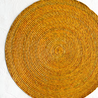 Ochre: A round woven straw placemat in ochre color.