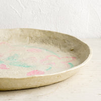 2: A round paper mache tray with faded pink and green design.