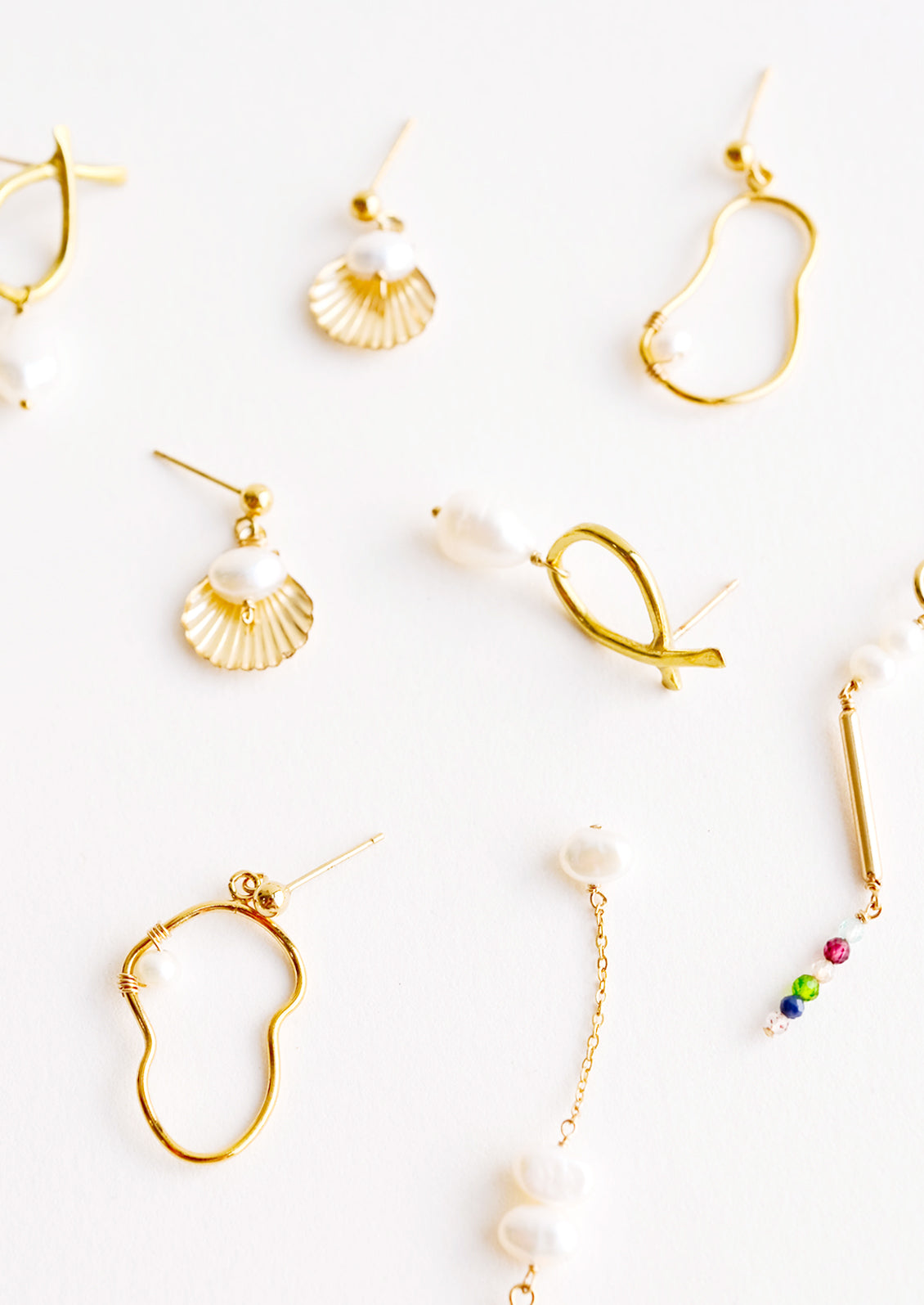 Product shot showing multiple styles and shapes of brass earrings with pearls.
