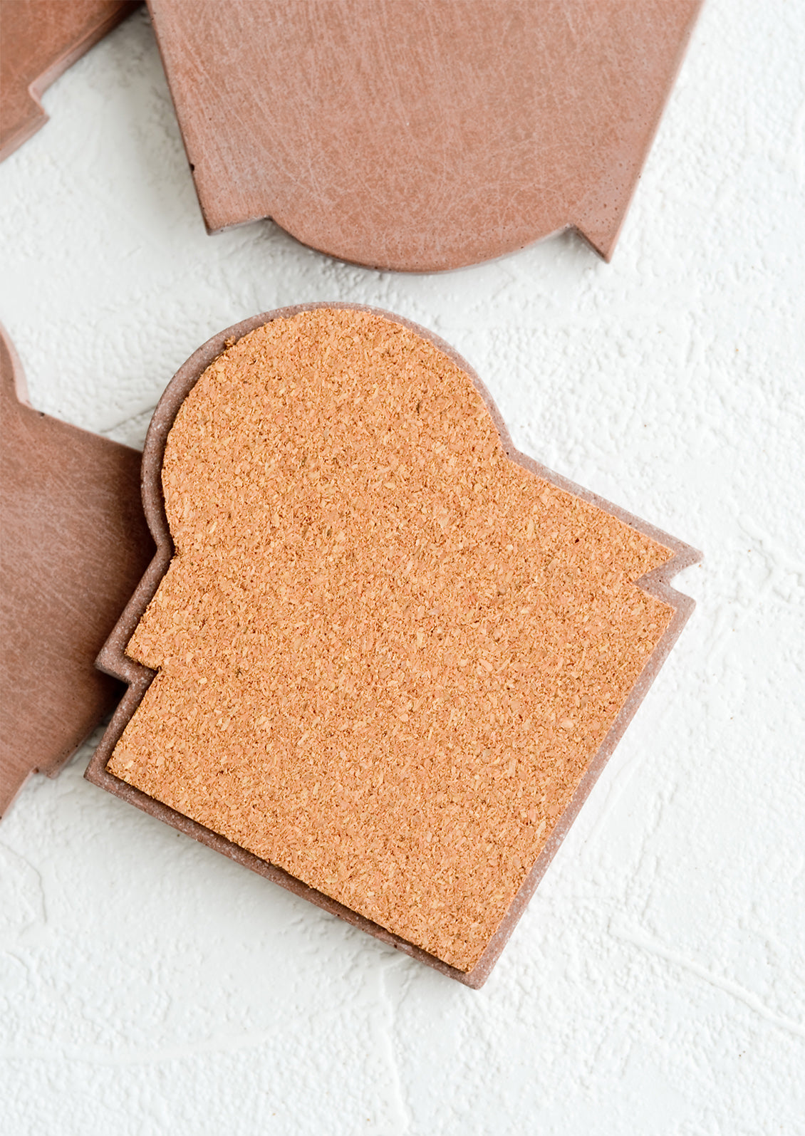 An abstract shaped concrete coaster with protective cork backing.