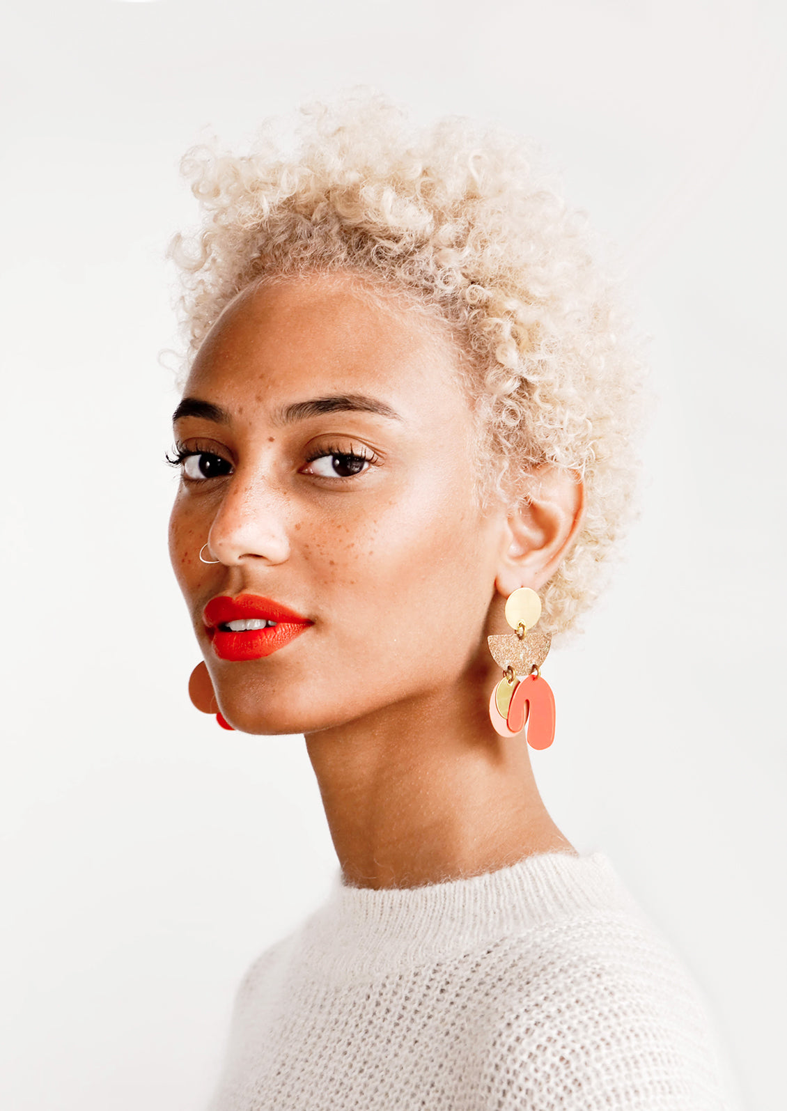Model wears orange and gold earrings with white top.