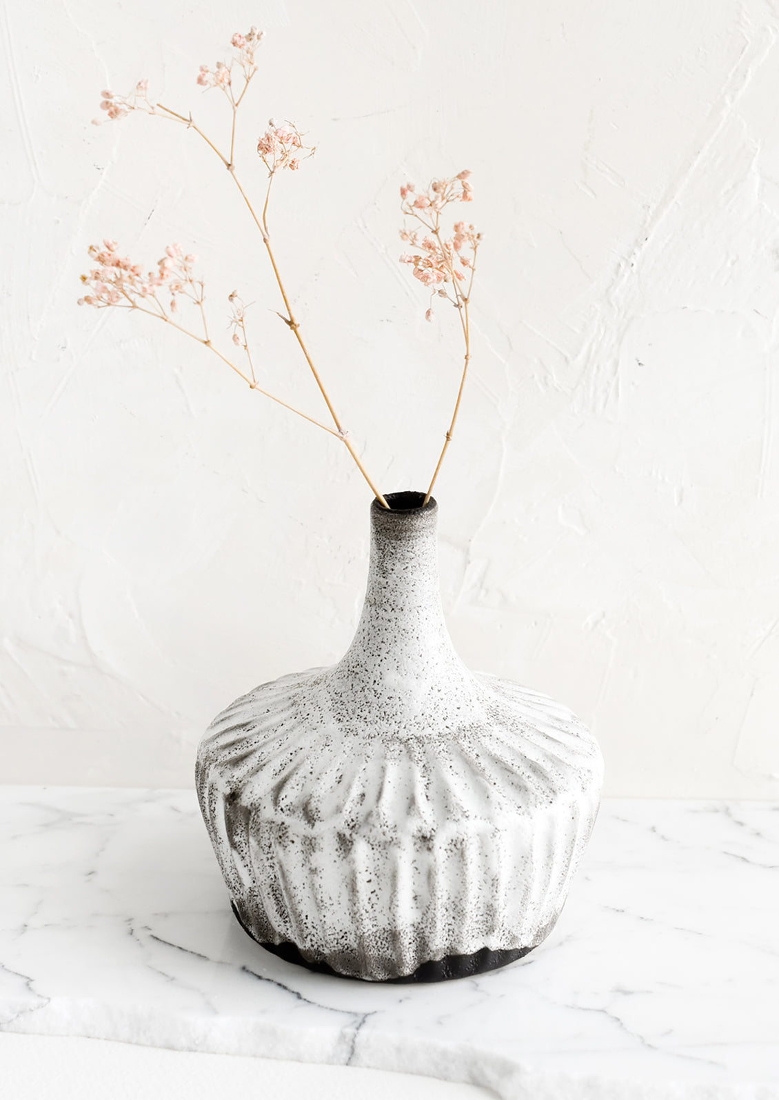 A ceramic vase in rustic white glaze over dark clay, with dried pink flower.