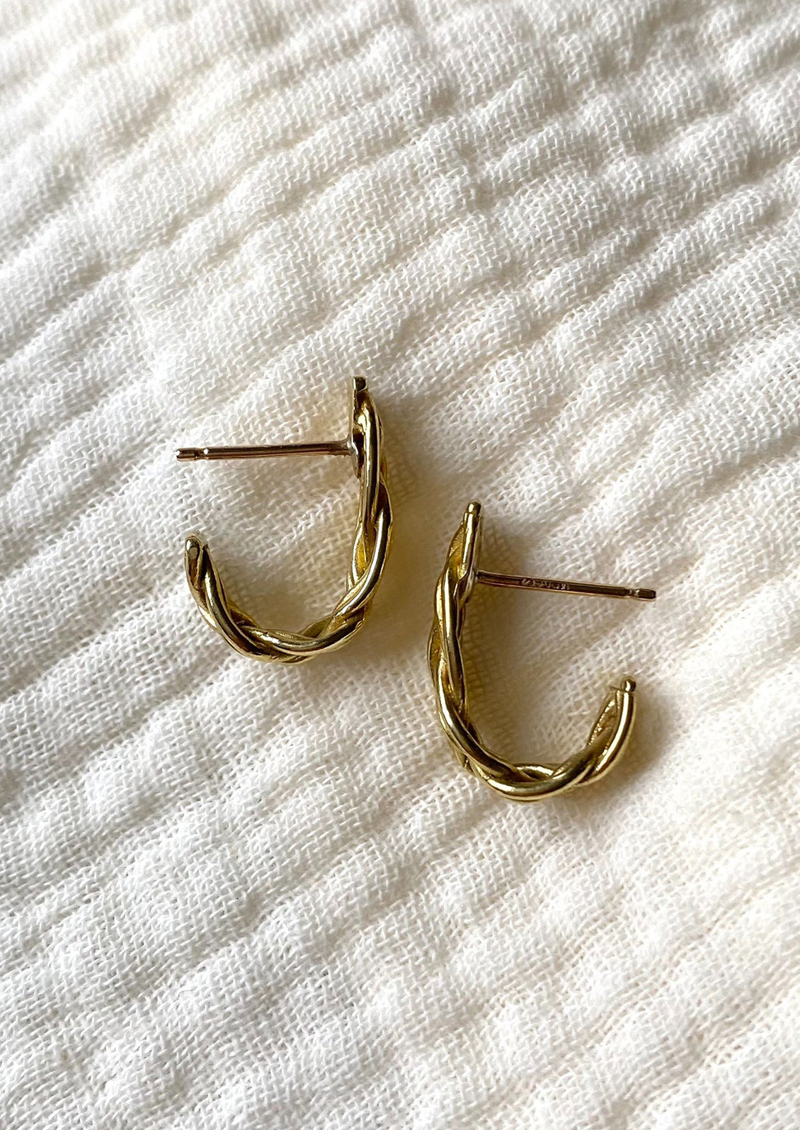 A pair of braided brass earrings that curve at bottom.