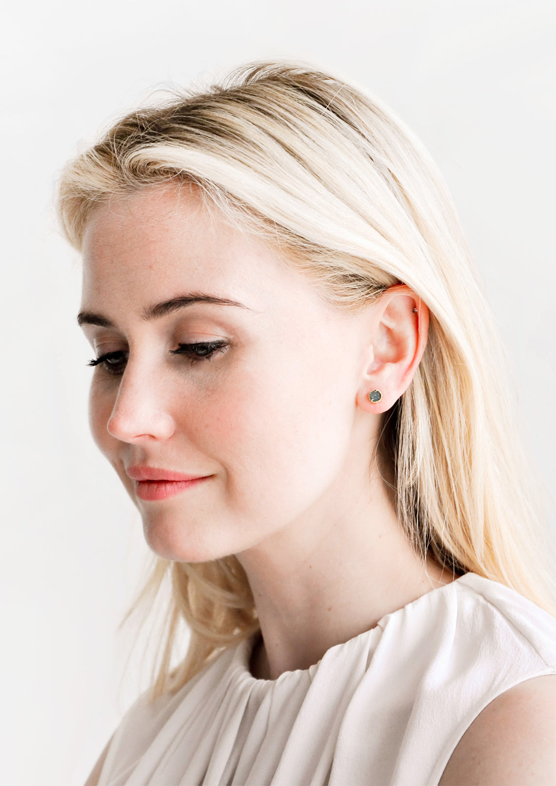 Model wears stud earrings with ivory blouse