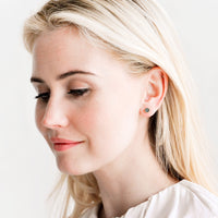 4: Model wears stud earrings with ivory blouse