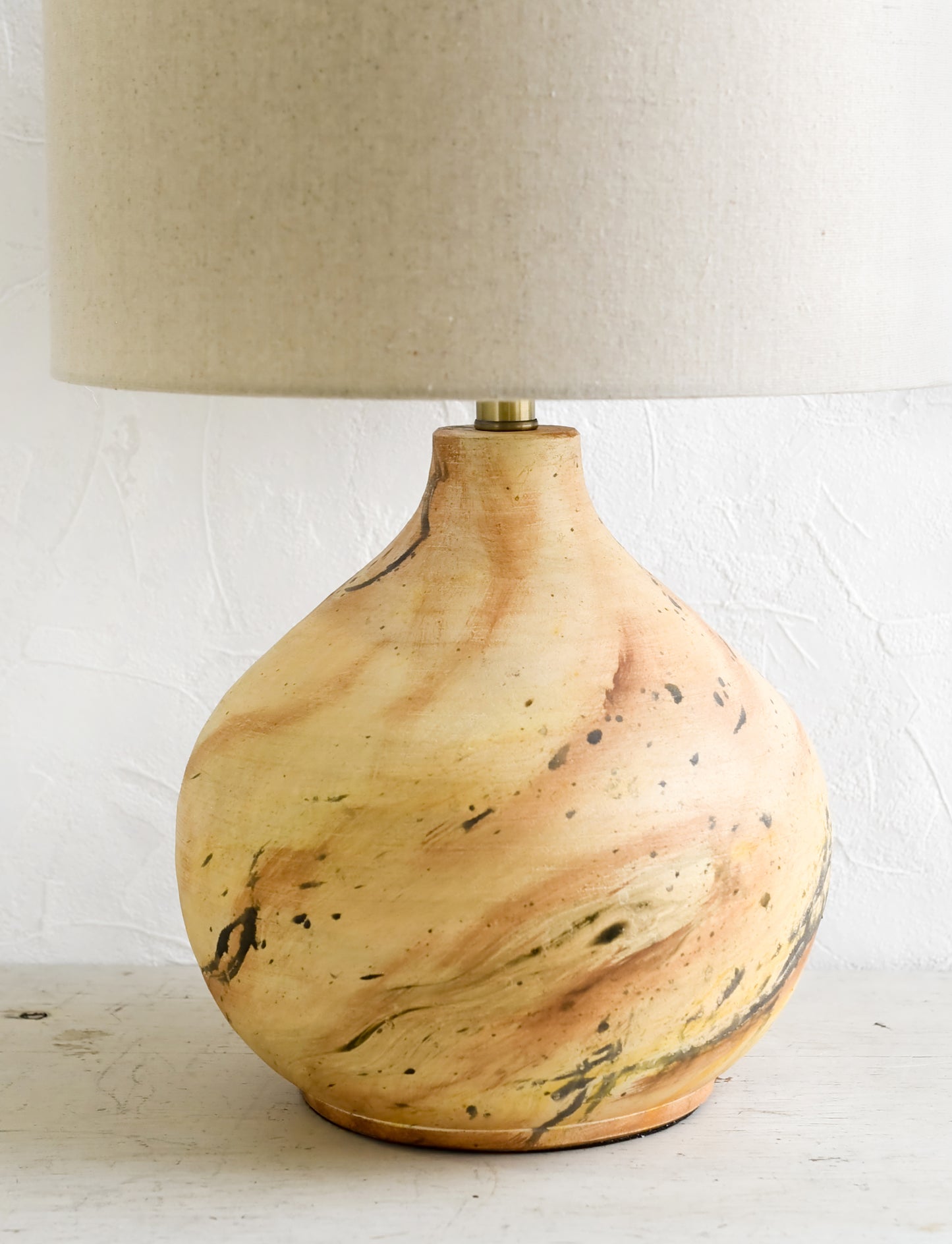 A table lamp with round ceramic base with paint splatter effect and round natural linen shade.