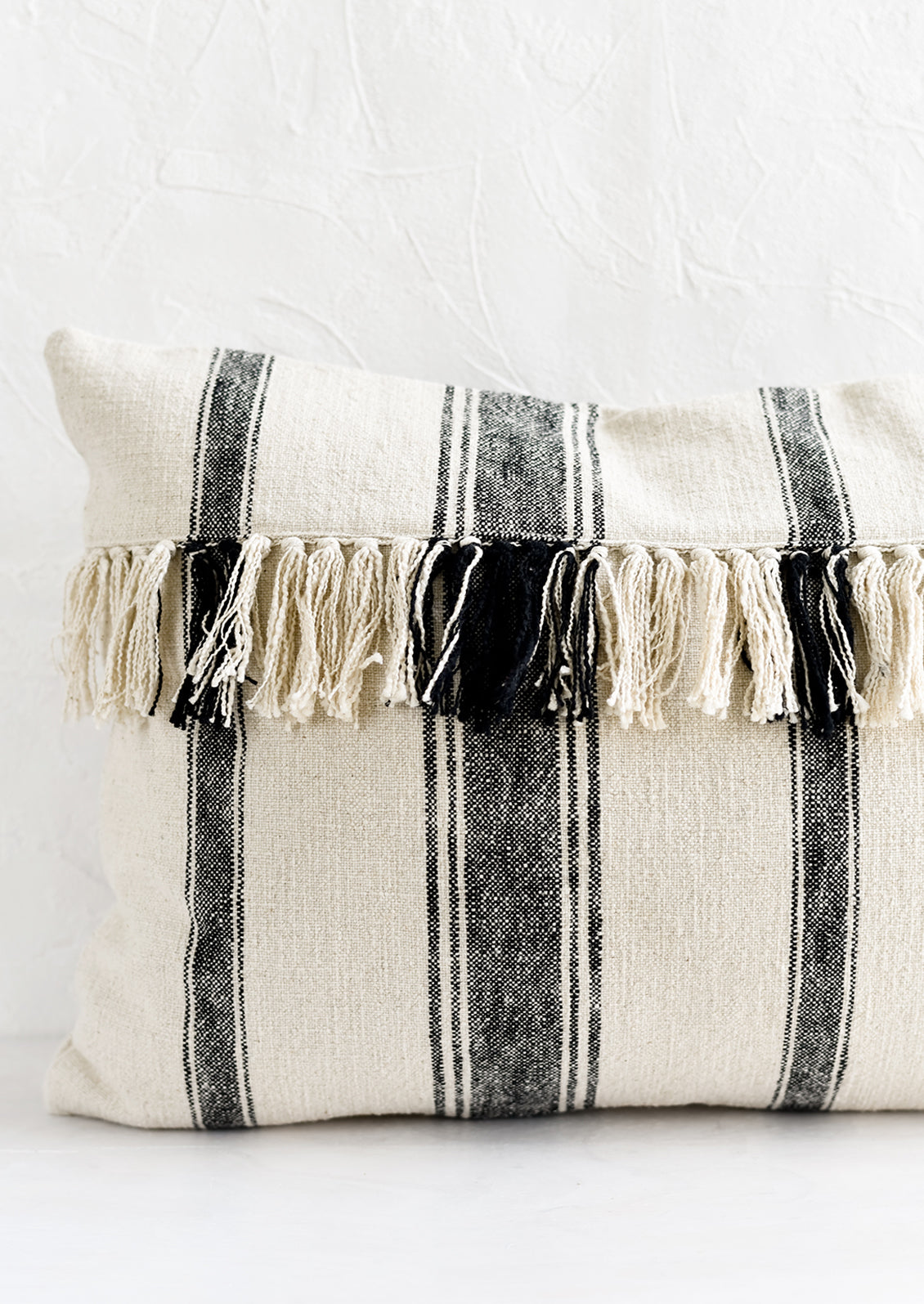 A lumbar throw pillow in natural cotton with vertical black stripes and horizontal fringe.