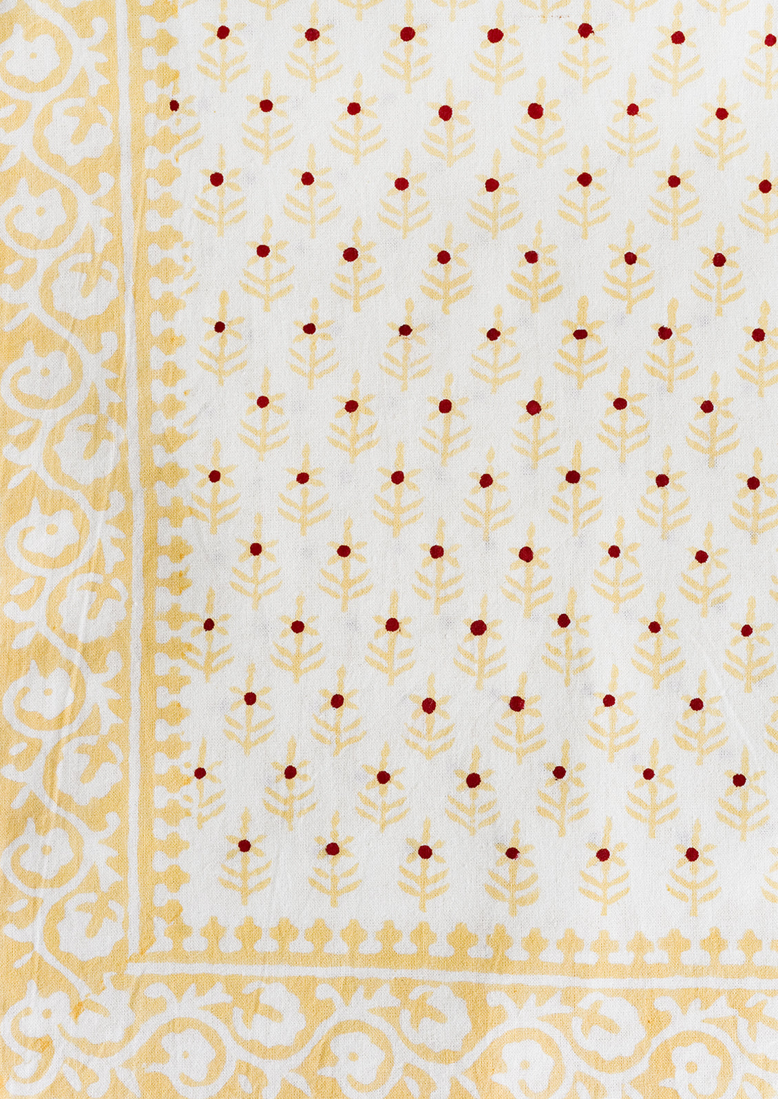 A cotton tablecloth in yellow and red floral block print motif.