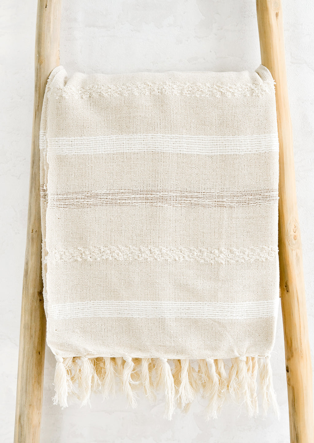 White Multi: A woven cotton gauze blanket with textured stripes in white on a display ladder.
