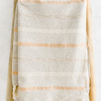 Apricot Multi: A woven cotton gauze blanket with textured stripes in apricot on a display ladder.