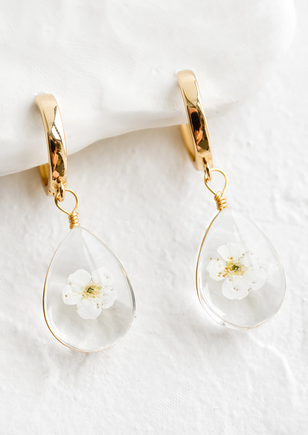 White: A pair of earrings with gold huggie hoop and clear resin drop with encased white florals.