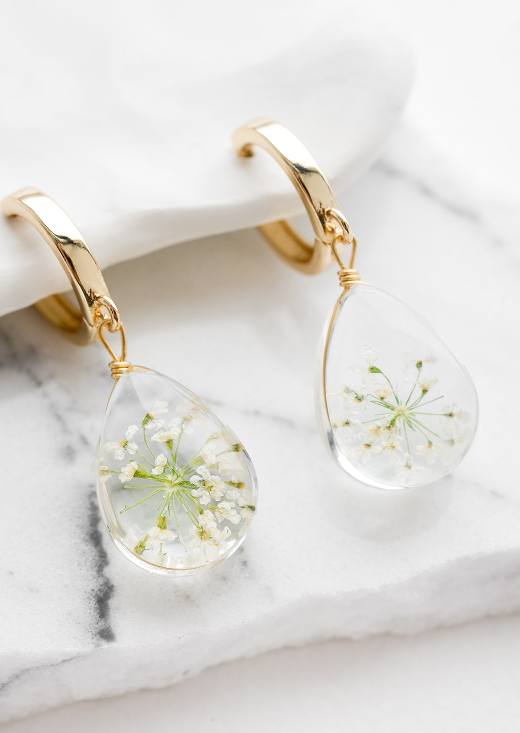 White / Green: A pair of earrings with gold huggie hoop and clear resin drop with encased white and green florals.