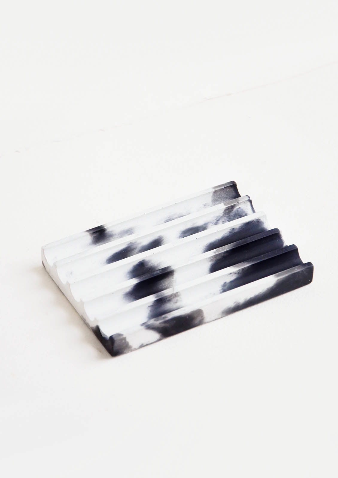A marbled black and white smooth concrete soap dish with troughs and ridges.