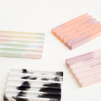 2: Four smooth concrete ridged soap dishes in rainbow, coral, pink, and black and white.