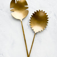 1: A pair of salad servers made from antiqued brass, shaped in a prehistoric-inspired design.