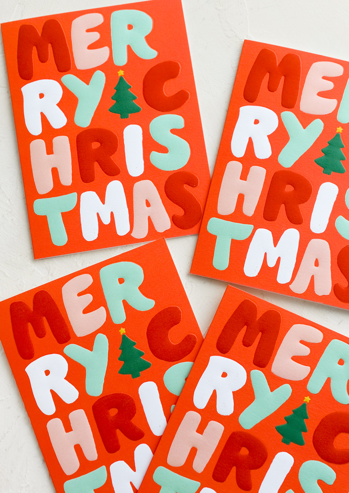 A red card set with red, white and green raised lettering reading "Merry Christmas".