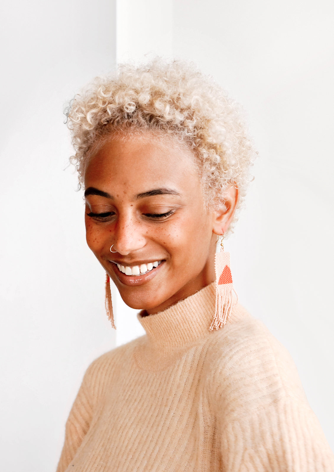 Model wears peach and orange fringe beaded earrings and peach colored sweater.