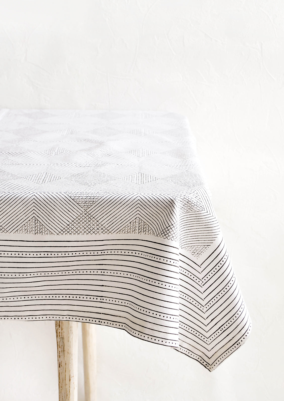 Black and white cotton tablecloth with geometric line and diamond print, displayed on a table