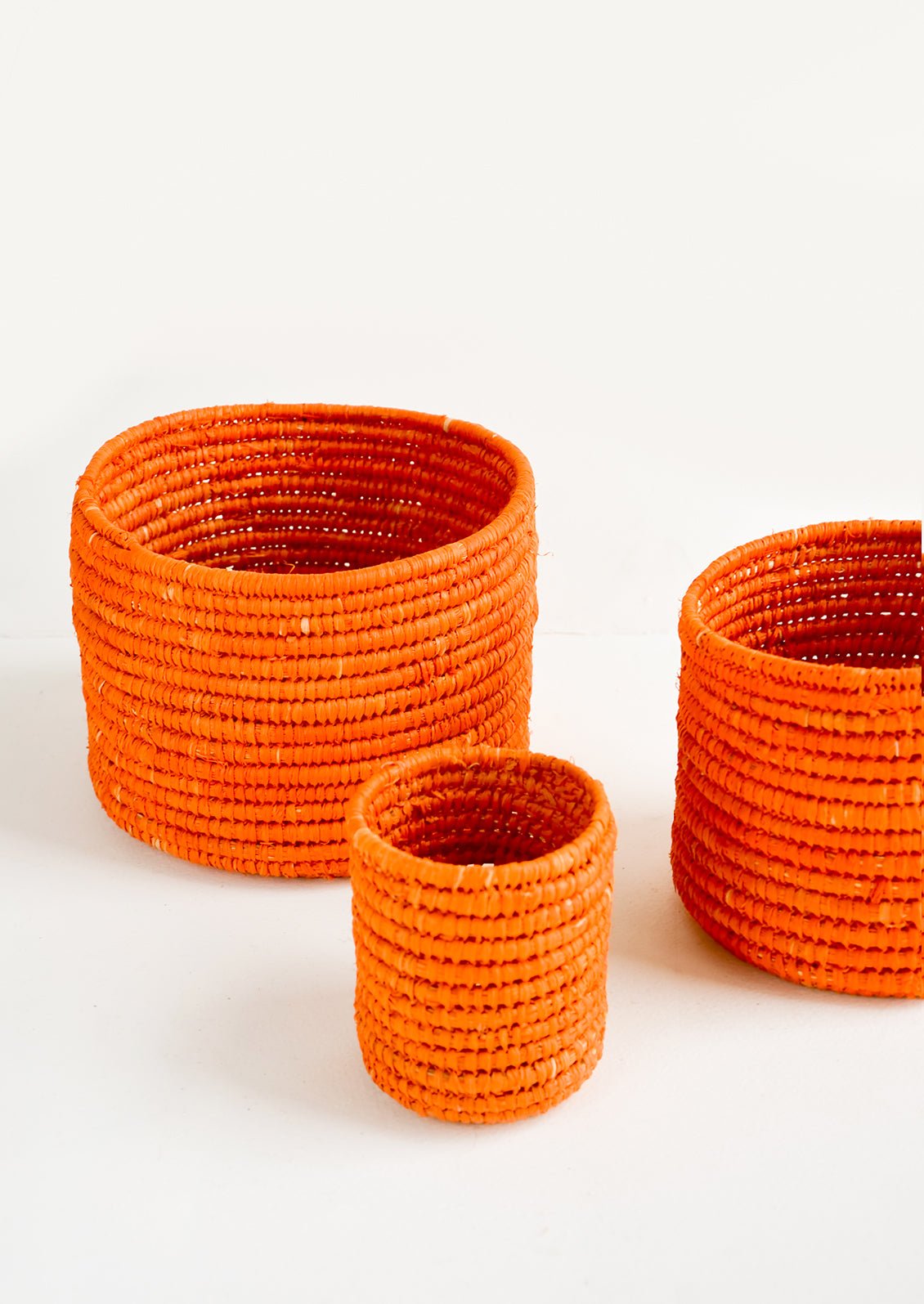 Set of round catchall baskets made from orange raffia in three incremental sizes.