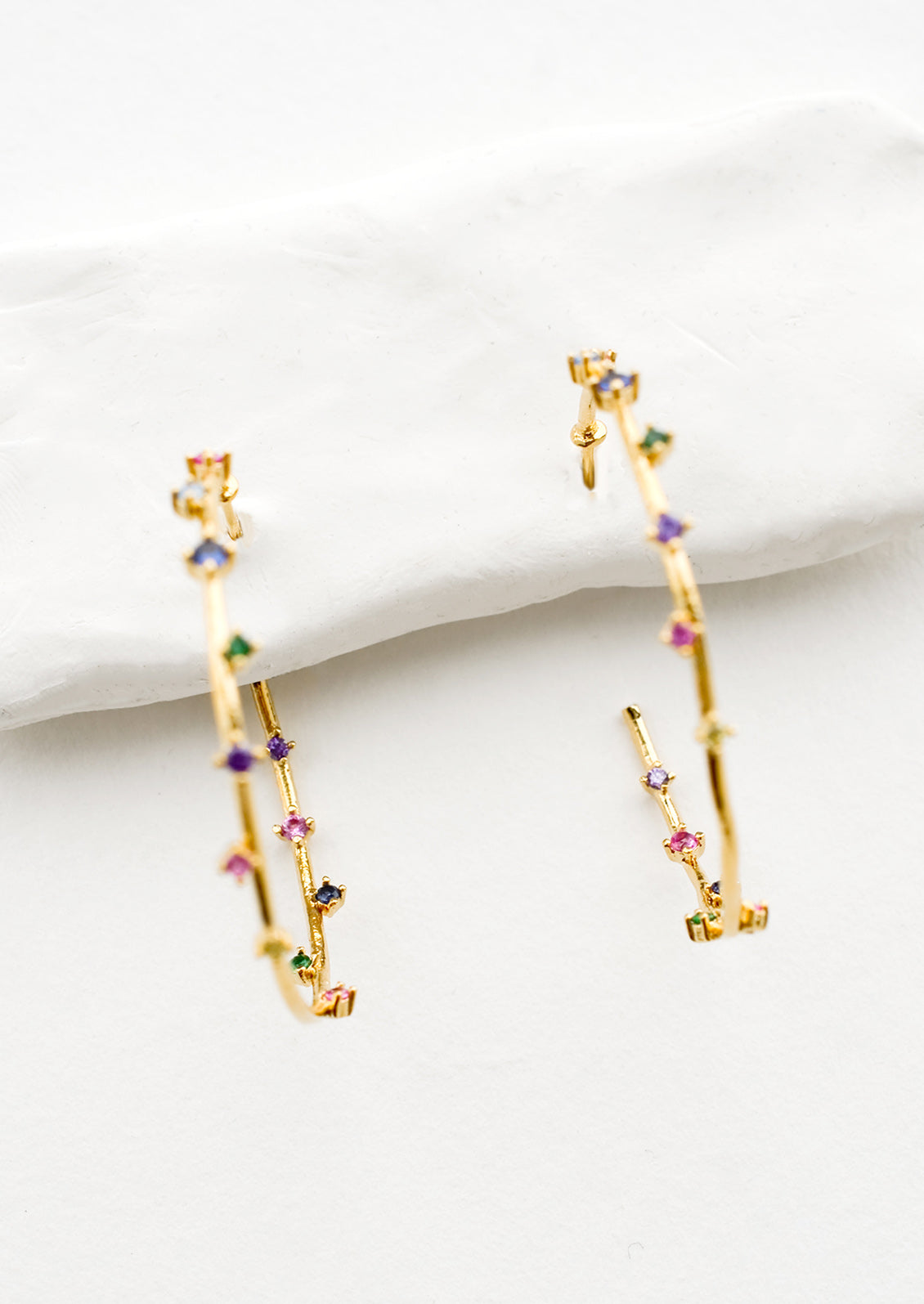 A pair of gold hoop earrings with colored crystals wrapping around the hoop sporadically.