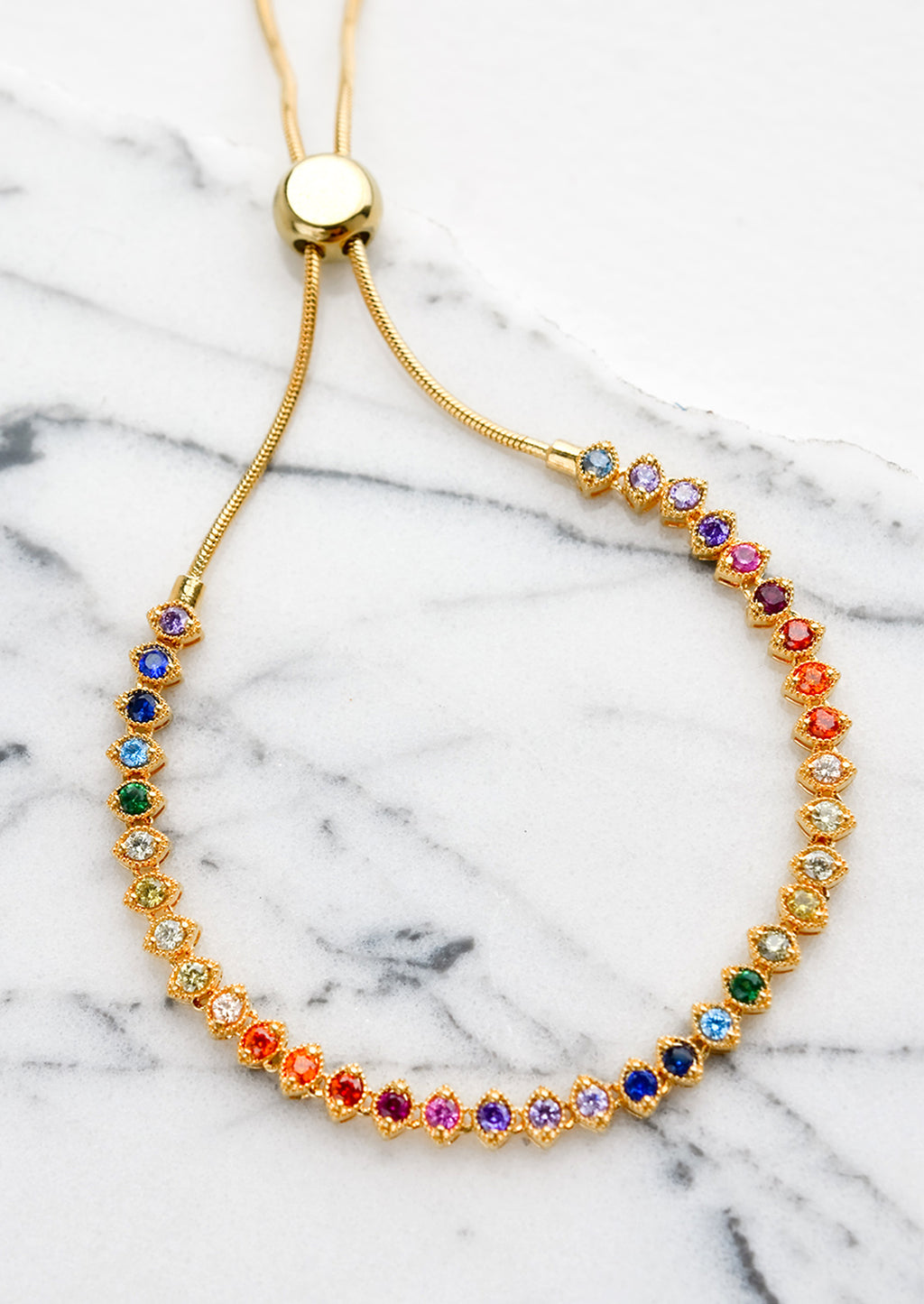 1: A gold, tennis style bracelet with marquis shaped crystals in rainbow color span.