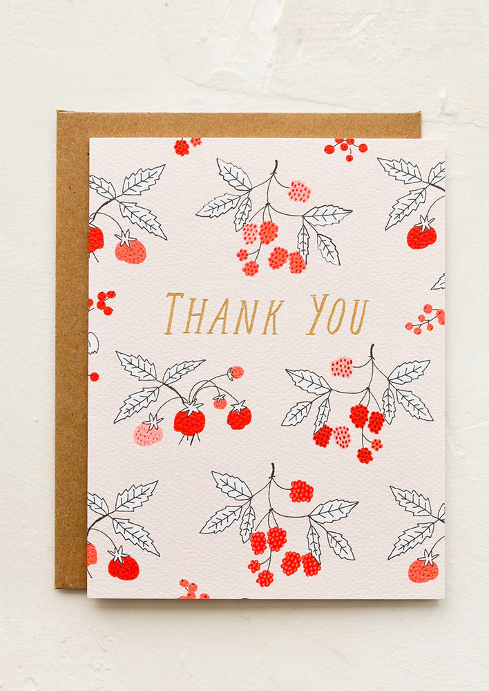 A greeting card with raspberry print and "Thank you" gold lettering.