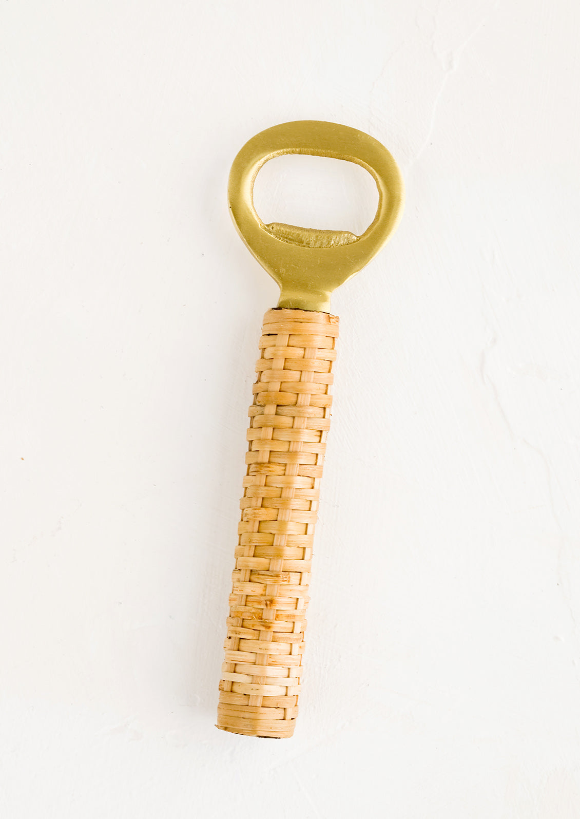 A brushed brass metal bottle opener with rattan wrapped handle.